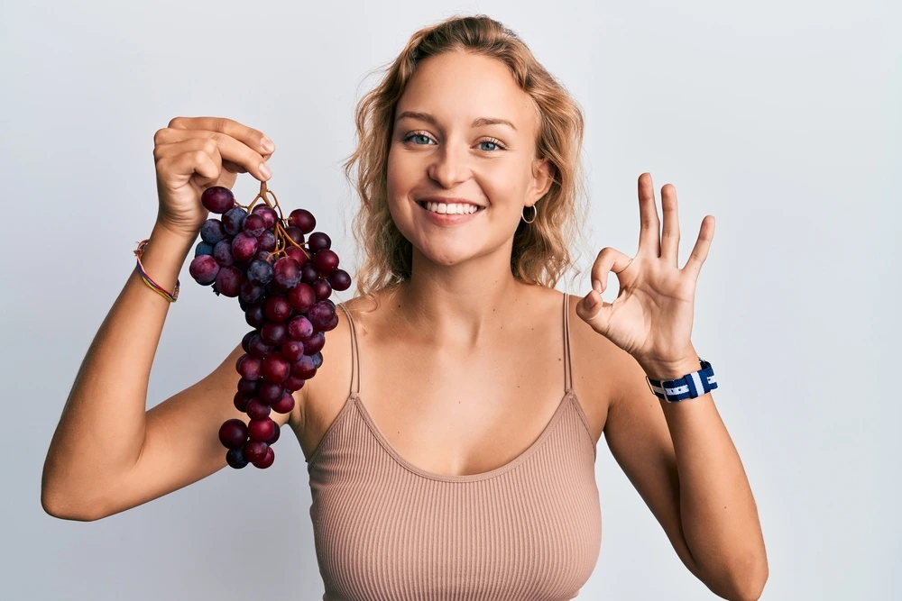 Cute girl holding a cluster of red grapes while smiling and giving an 'okay' symbol