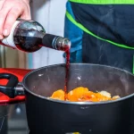 Man pouring dry red wine into pot while cooking
