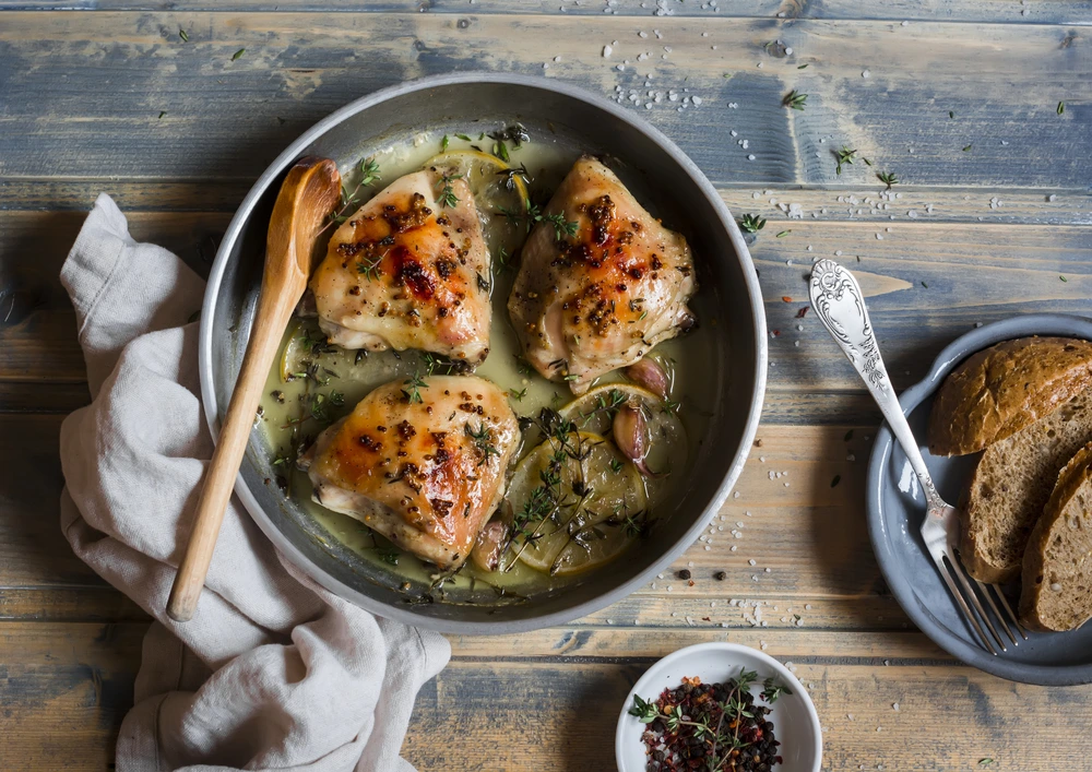 Baked chicken in white wine in the pan on wooden table
