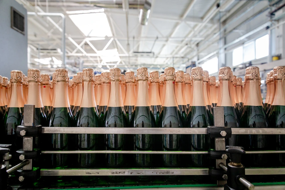 Bottles of sparkling champagne wine lined up on a convyer belt production method