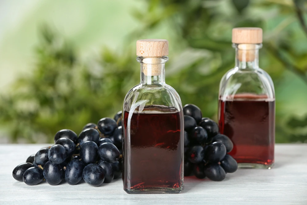 Red Wine Vinegar in bottles with grapes sitting on a wooden table