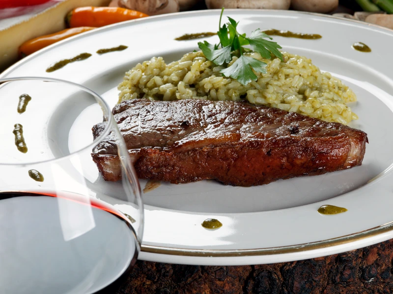 Red meat and rice on a plate served with red wine closeup