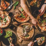 People eating different kinds of pizza, salad and drinking wine closeup