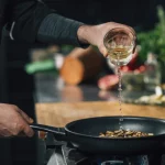 Chef pouring white wine into a frying pan with mushrooms