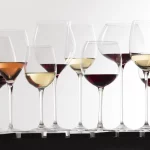 Different types of wine lined up in glasses on a white background