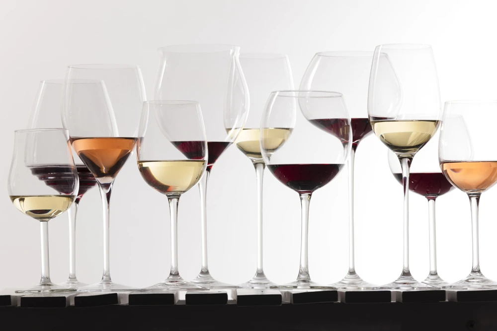 Different types of wine lined up in glasses on a white background