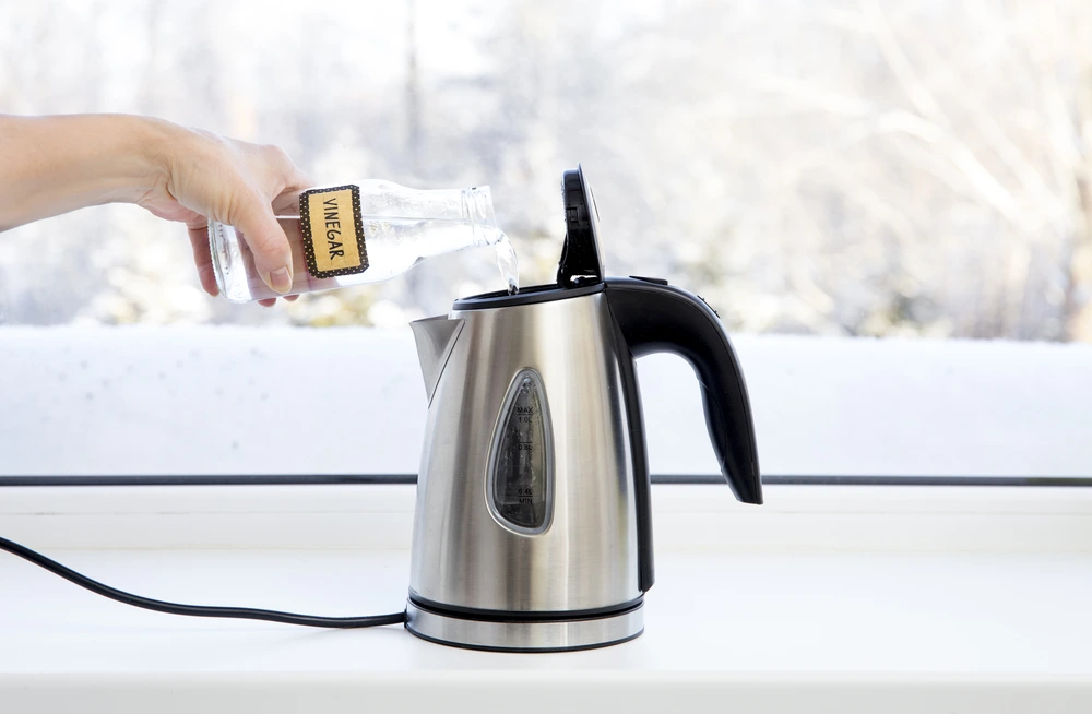 Woman pouring white vinegar into a kettle to clean it