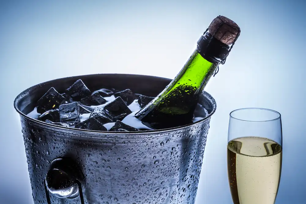Champagne in an ice bucket with flute closeup on a somber blue background