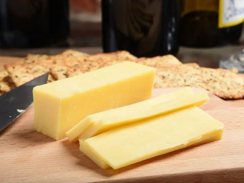 Cheddar cheese sliced up on a chopping board with red wine