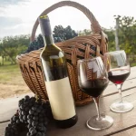 Two glasses of red wine with a bottle, black grapes and a picnic basket