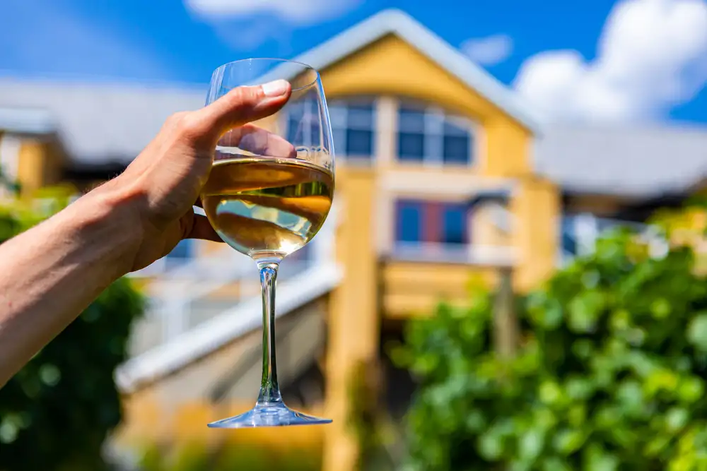 Glass of Pinot Grigio being held up in front of a tasting house.