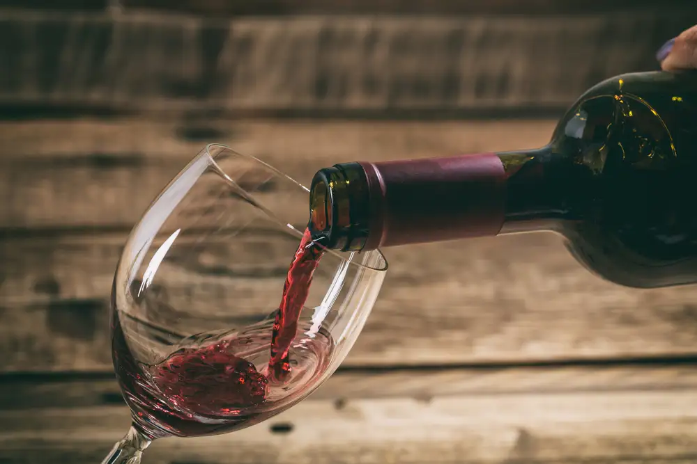 Pouring red wine in a glass on wooden background close up