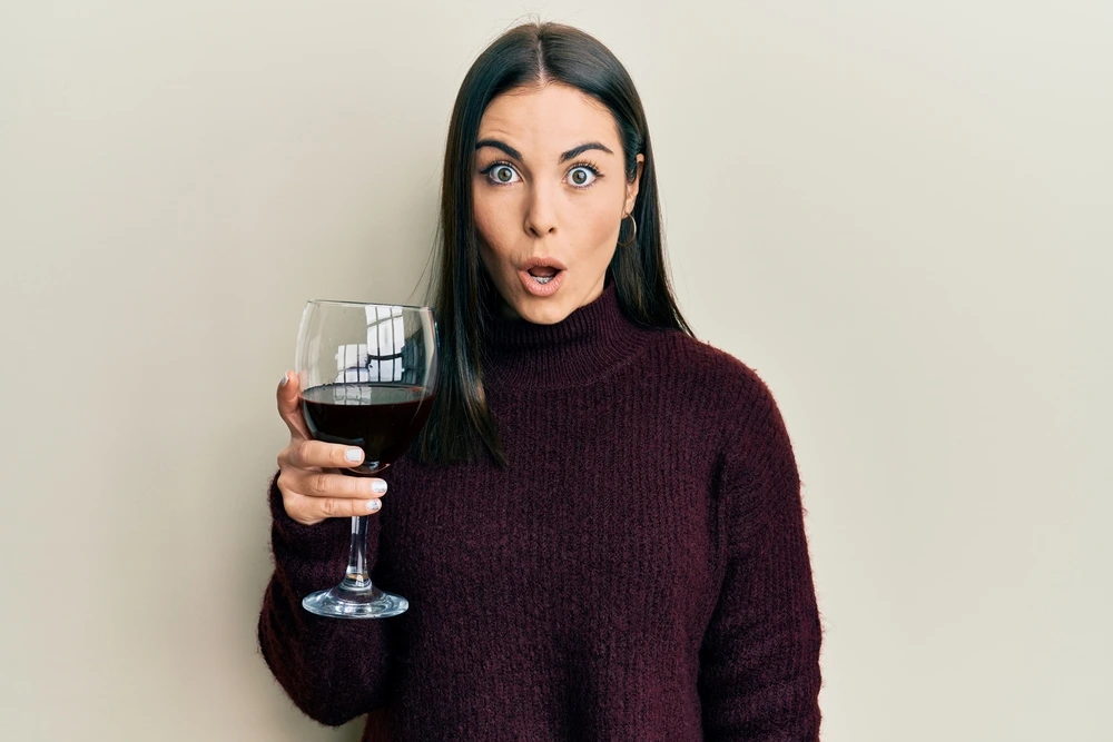 Beautiful brunette holding a glass of red wine with a surprised look on her face