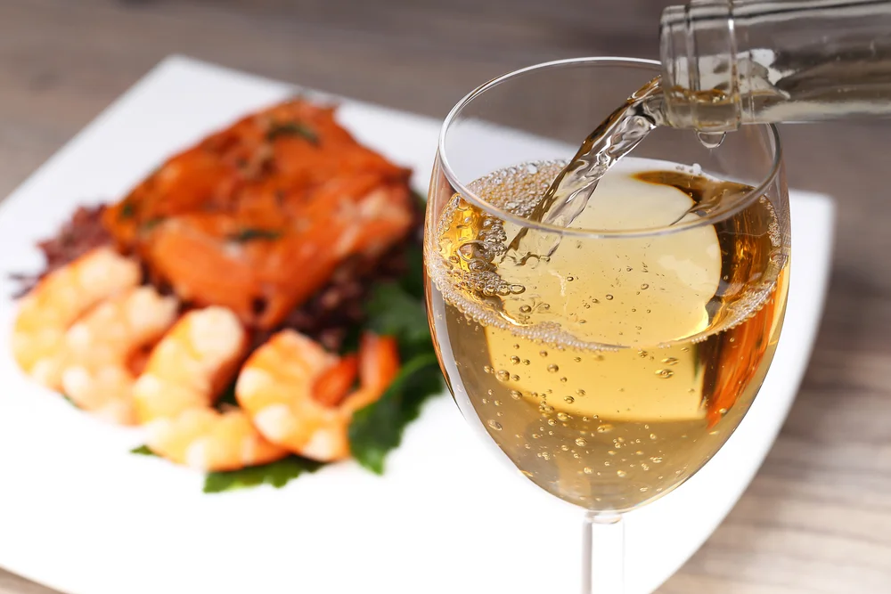 White wine being poured into a glass with seafood in the background close-up