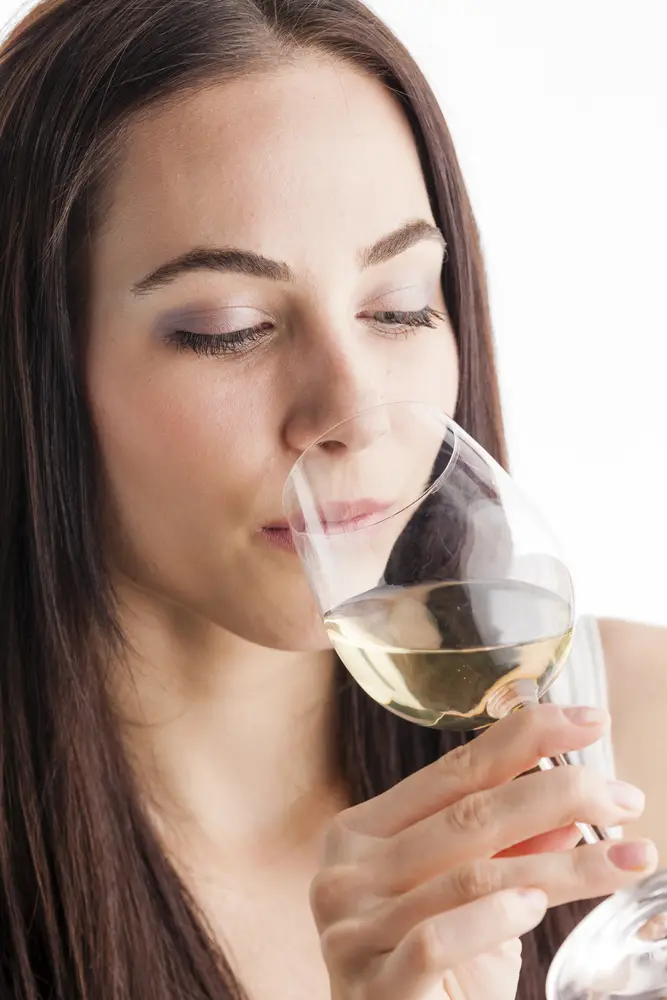 Young brunette Woman tasting white wine with a white background